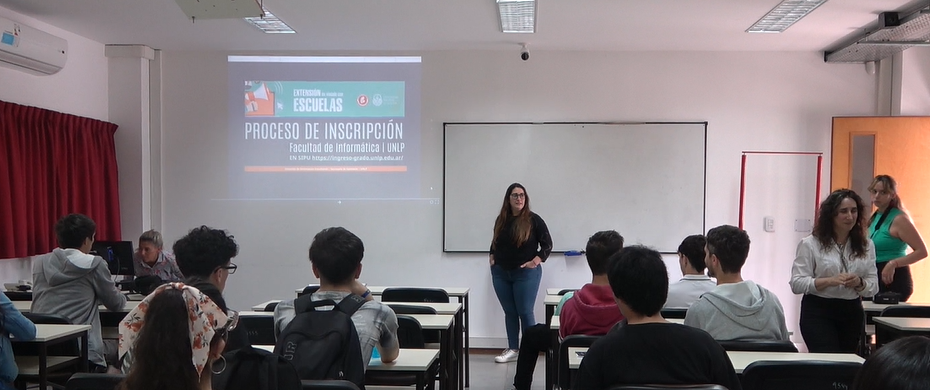 Espacio aúlico en la Facultad de Informática con ingresantes sentados en los bancos mirnado una presentación a cargo de una responsable