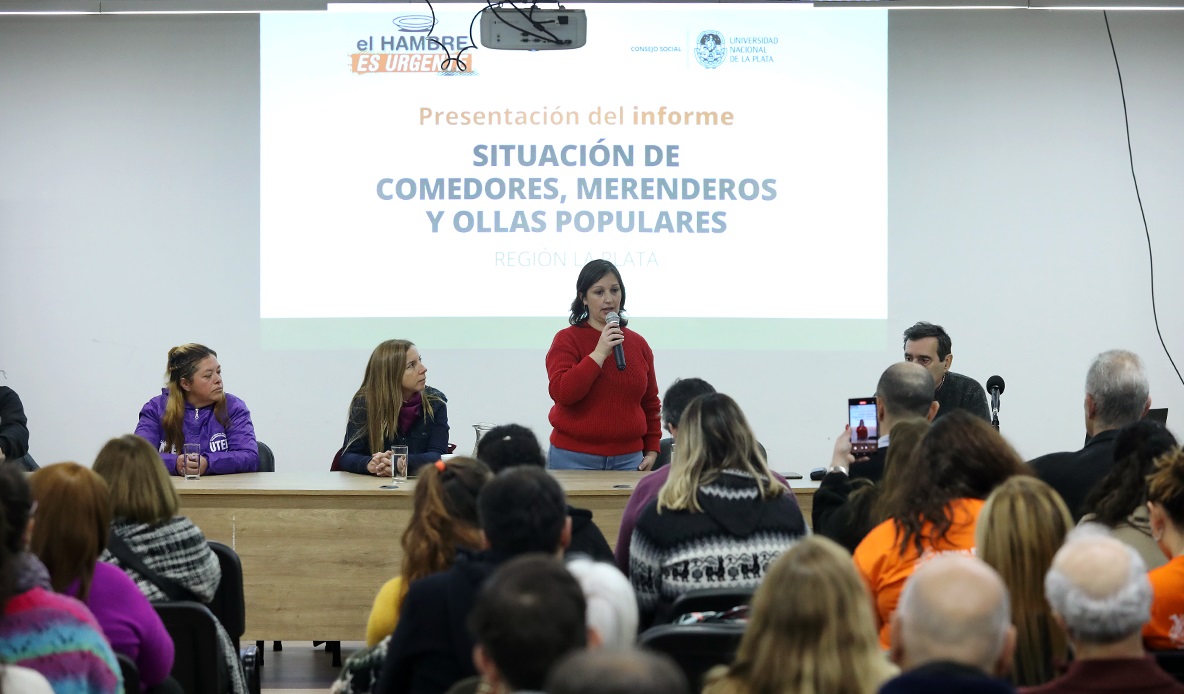 Imagen del aula del aula 201 del Edificio Karacachoff en la presentación del informe de situación de comedores, merenderos y ollas populares de la región La Plata. Ubidada de frente y de pie Inés iglesias a cargo del Consejo Social de la UNLO expone con midrófono en mano ante un nutrida concurrencia