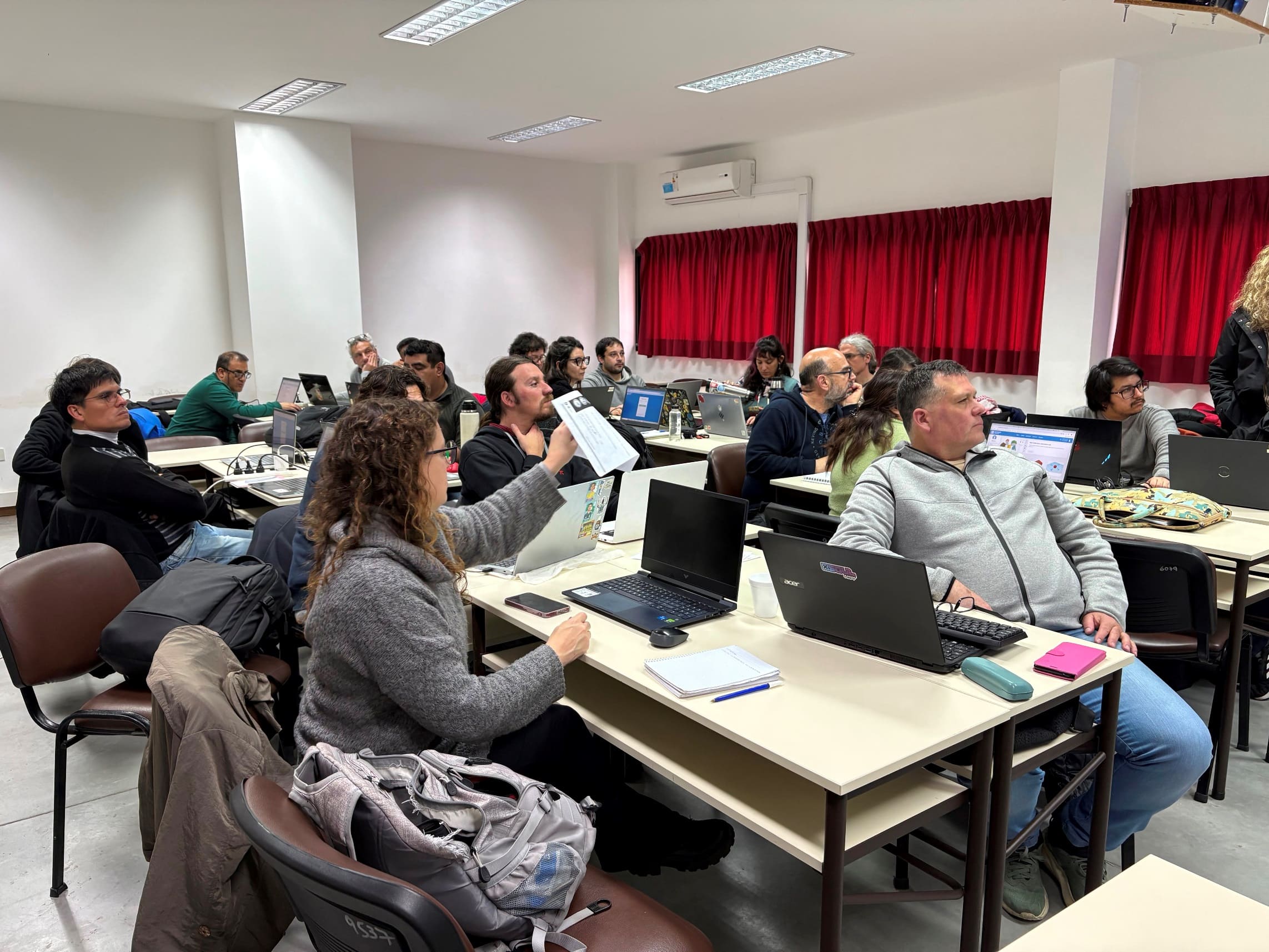 Banner colorido con ilustraciones de jóvenes moviéndose; título en blanco sobre una forma geométrica: El barrio va a la Universidad: Alfabetización Digital y Lectoescritura.